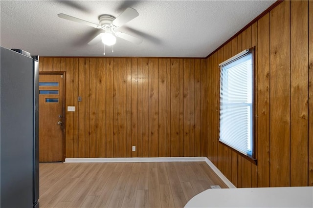 unfurnished bedroom featuring multiple windows, a textured ceiling, stainless steel refrigerator, and light hardwood / wood-style floors