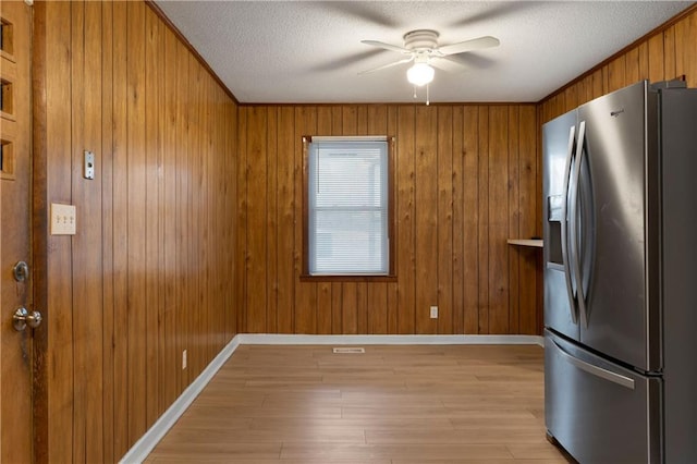 kitchen featuring wood walls, stainless steel fridge with ice dispenser, light hardwood / wood-style flooring, a textured ceiling, and ceiling fan