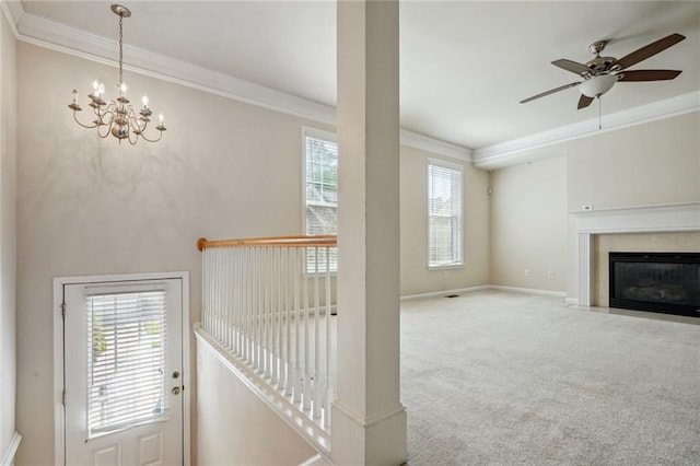 unfurnished living room featuring baseboards, a fireplace with flush hearth, carpet floors, ornamental molding, and ceiling fan with notable chandelier