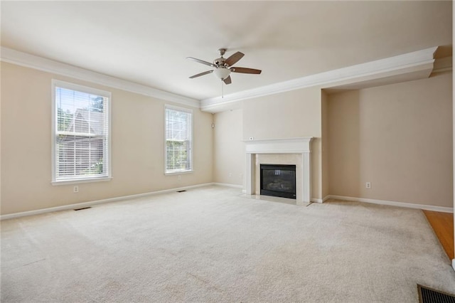 unfurnished living room featuring ceiling fan, a tiled fireplace, plenty of natural light, and ornamental molding