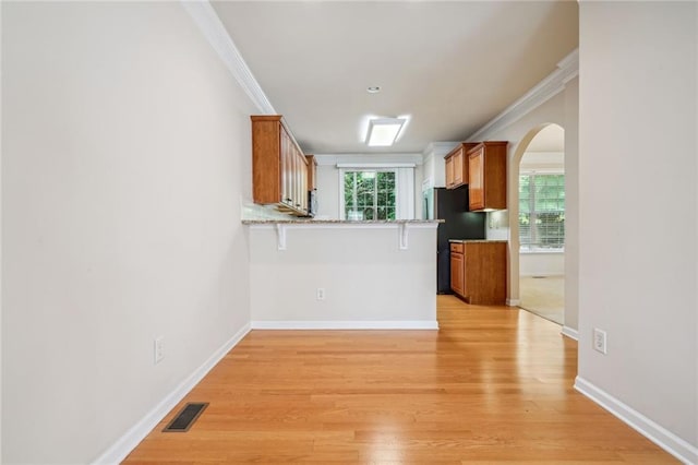 kitchen featuring black fridge, a kitchen bar, light hardwood / wood-style floors, kitchen peninsula, and crown molding