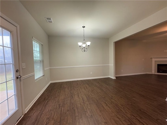 unfurnished dining area featuring a notable chandelier, a fireplace, visible vents, baseboards, and dark wood-style floors