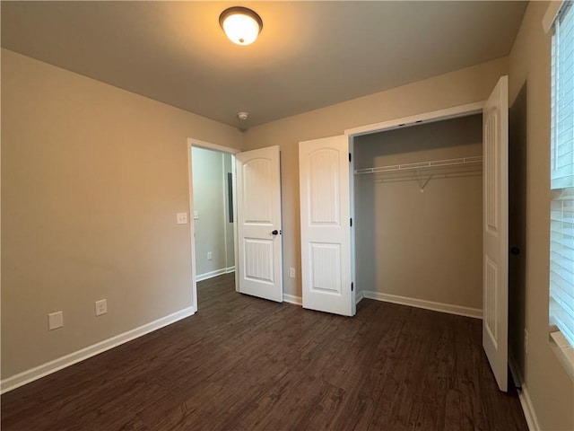 unfurnished bedroom with dark wood-style floors, a closet, and baseboards