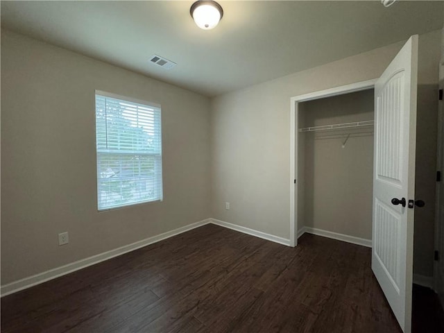 unfurnished bedroom with a closet, dark wood finished floors, visible vents, and baseboards