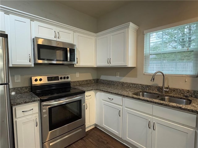 kitchen with white cabinets, appliances with stainless steel finishes, dark wood-style flooring, dark stone countertops, and a sink