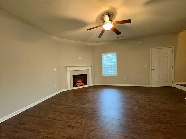 unfurnished living room featuring dark wood-style floors, ceiling fan, a warm lit fireplace, and baseboards