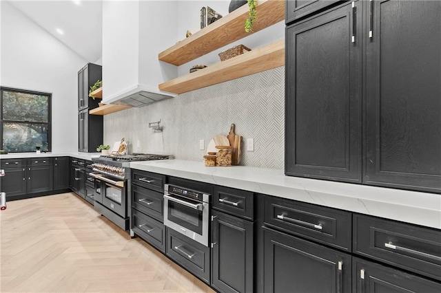 kitchen featuring light stone counters, open shelves, decorative backsplash, appliances with stainless steel finishes, and dark cabinets