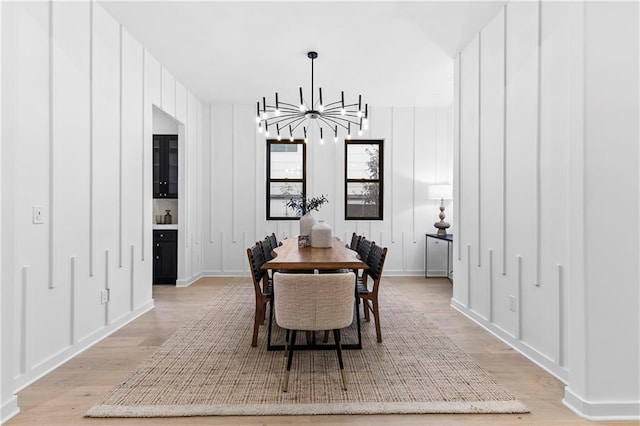 dining room featuring an inviting chandelier, a decorative wall, and light wood-style floors