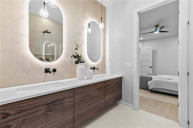 bathroom featuring connected bathroom, ceiling fan, double vanity, tiled shower, and a sink