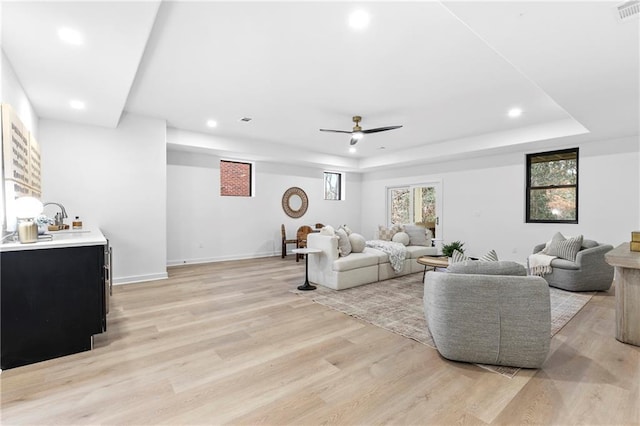 living area with a tray ceiling, light wood-style flooring, ceiling fan, and recessed lighting