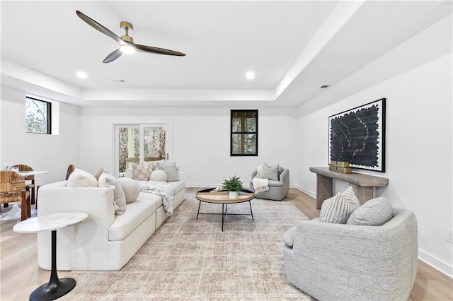 living room with recessed lighting, a tray ceiling, ceiling fan, and light wood-style flooring