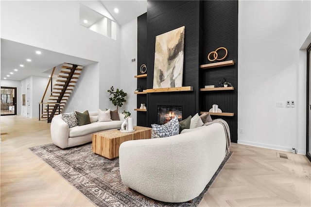 living area featuring visible vents, baseboards, recessed lighting, a towering ceiling, and a glass covered fireplace