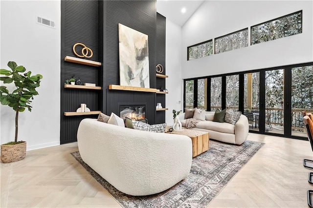 living room featuring visible vents, baseboards, recessed lighting, a glass covered fireplace, and high vaulted ceiling