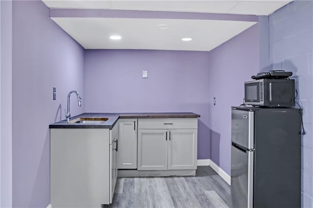 kitchen featuring dark countertops, light wood-style floors, freestanding refrigerator, white cabinetry, and a sink