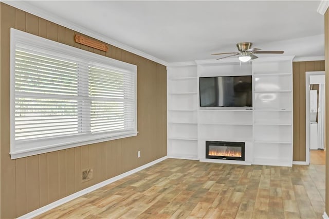 unfurnished living room with built in features, crown molding, a ceiling fan, a glass covered fireplace, and wood finished floors