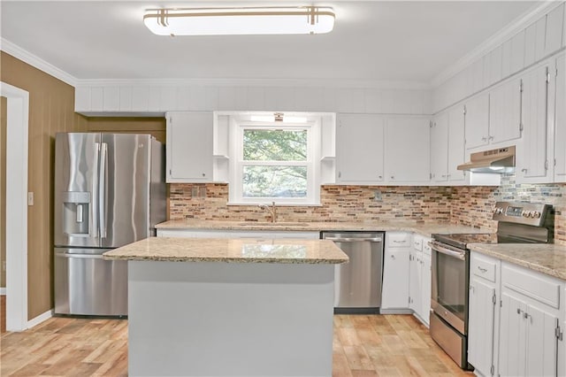 kitchen with light wood-style floors, appliances with stainless steel finishes, crown molding, under cabinet range hood, and a sink