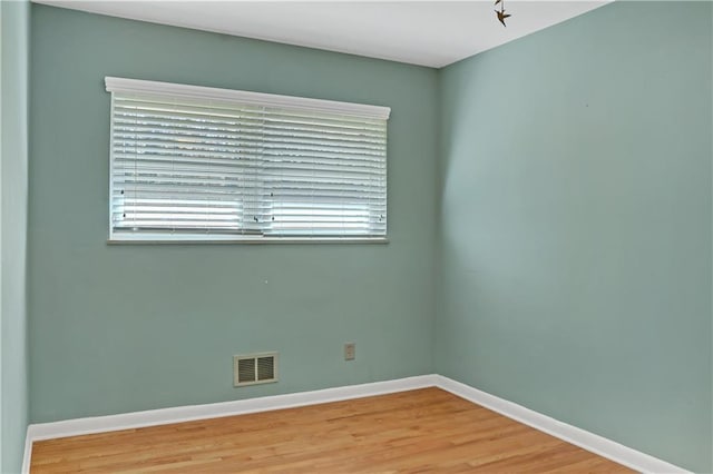 empty room with wood finished floors, visible vents, and baseboards