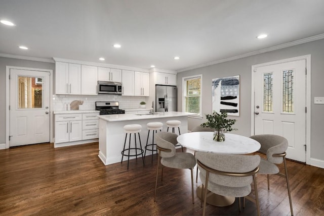 kitchen featuring dark wood-style floors, stainless steel appliances, ornamental molding, and a kitchen island with sink