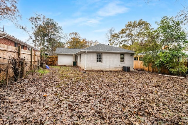 rear view of property with a fenced backyard, roof with shingles, cooling unit, and brick siding