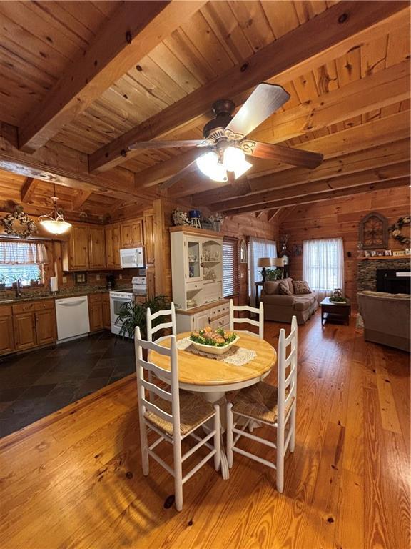 dining area featuring beam ceiling, wooden ceiling, ceiling fan, and wood walls