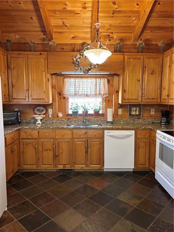 kitchen featuring stone counters, decorative light fixtures, sink, white appliances, and beam ceiling