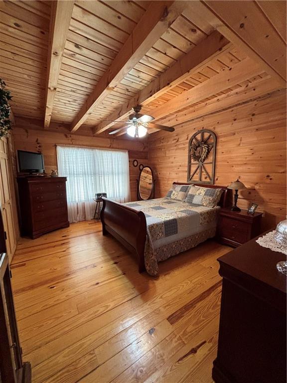 bedroom featuring beamed ceiling, wooden walls, wood ceiling, and ceiling fan