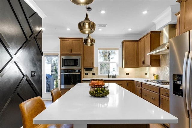 kitchen with appliances with stainless steel finishes, a kitchen breakfast bar, a kitchen island, decorative backsplash, and wall chimney exhaust hood