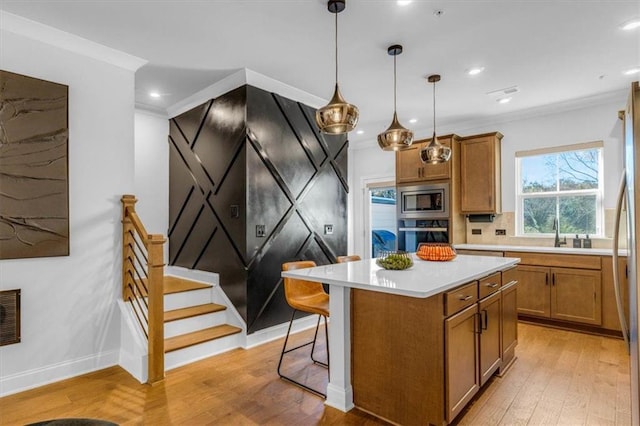 kitchen with decorative light fixtures, a center island, ornamental molding, appliances with stainless steel finishes, and light hardwood / wood-style floors