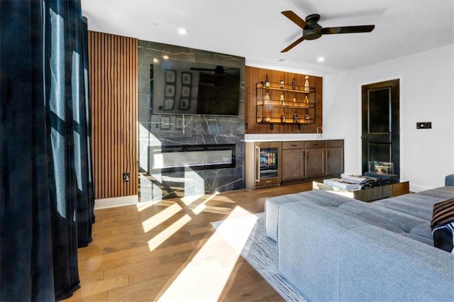 living room featuring light hardwood / wood-style flooring, ceiling fan, wine cooler, a high end fireplace, and bar area