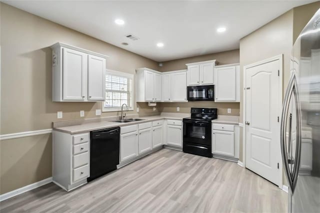 kitchen with visible vents, white cabinets, light countertops, black appliances, and a sink