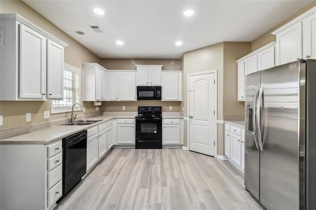 kitchen featuring light countertops, visible vents, white cabinets, a sink, and black appliances