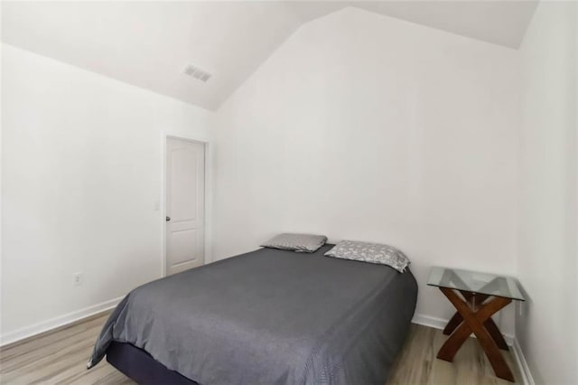 bedroom featuring light wood-style floors, lofted ceiling, visible vents, and baseboards