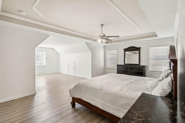 bedroom with a ceiling fan, a tray ceiling, baseboards, and wood finished floors