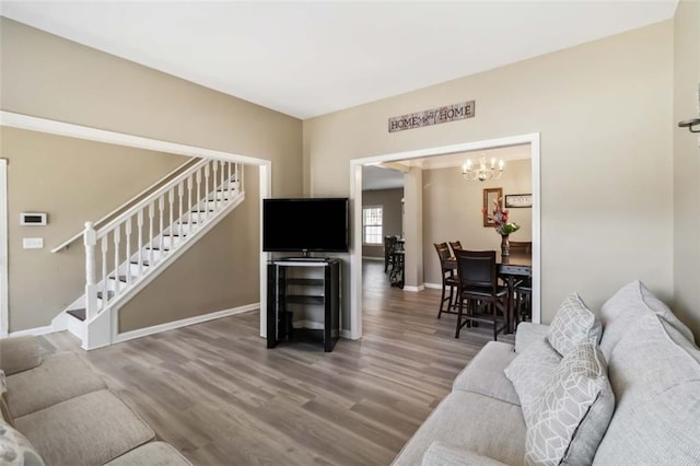 living area featuring a chandelier, stairway, baseboards, and wood finished floors