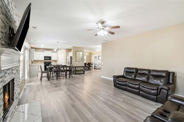 living room with a stone fireplace, visible vents, a ceiling fan, baseboards, and light wood finished floors