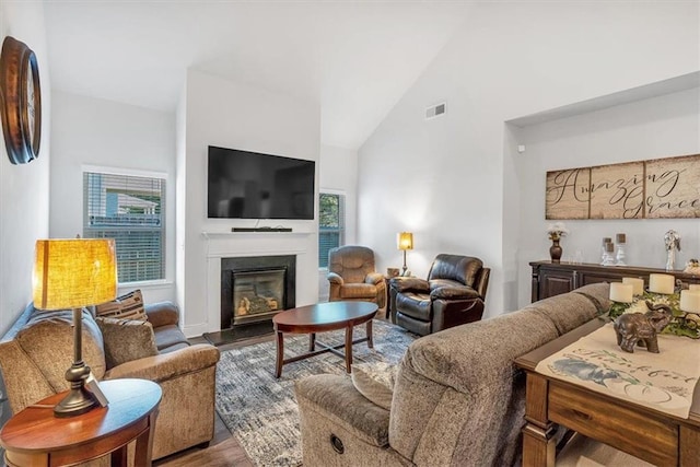 living area featuring visible vents, high vaulted ceiling, wood finished floors, and a fireplace