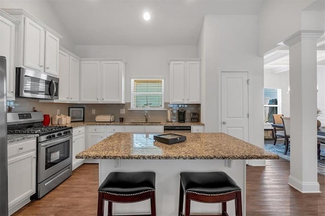 kitchen featuring a kitchen bar, decorative columns, white cabinetry, and appliances with stainless steel finishes