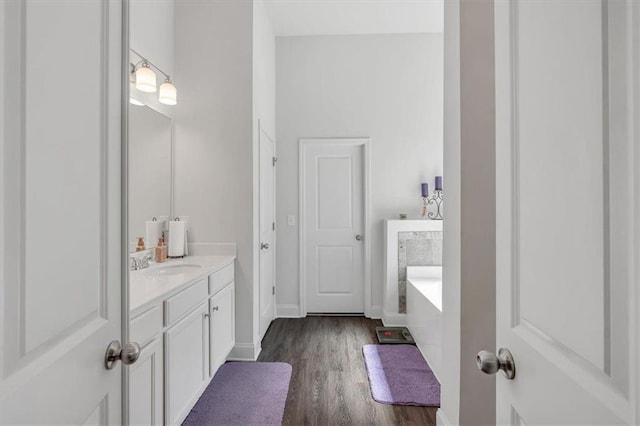 bathroom featuring vanity, a bath, wood finished floors, and baseboards