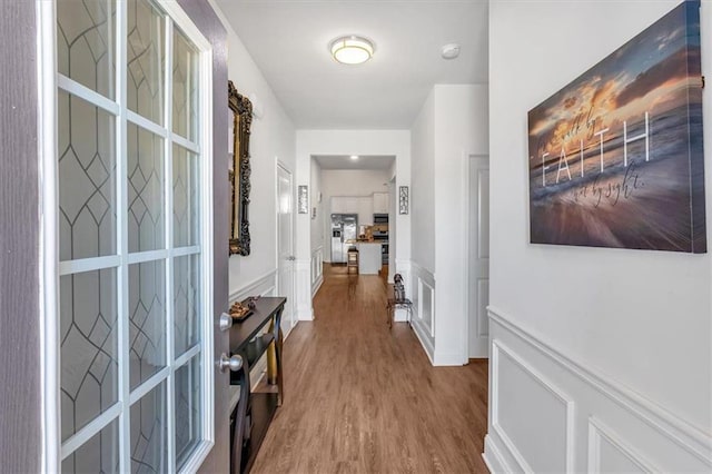 hallway featuring wood finished floors, wainscoting, and a decorative wall