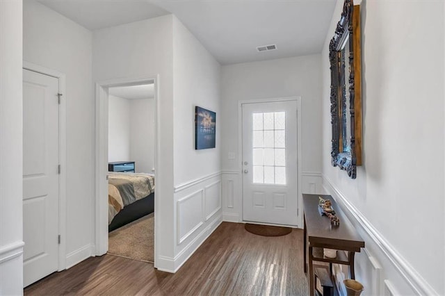 entryway featuring visible vents, wood finished floors, wainscoting, and a decorative wall