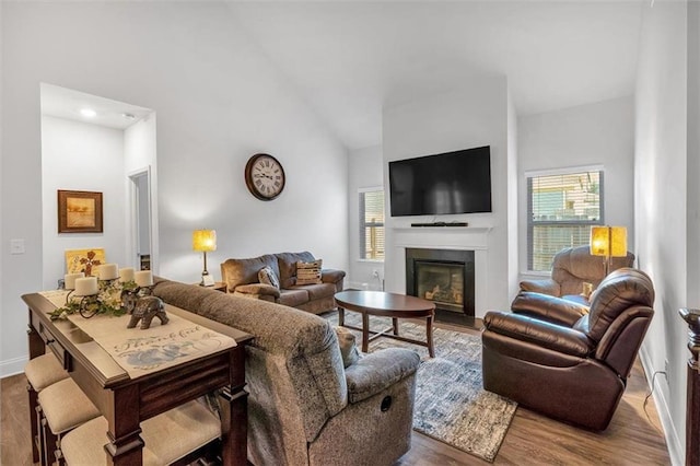 living area featuring baseboards, a fireplace with flush hearth, high vaulted ceiling, and wood finished floors