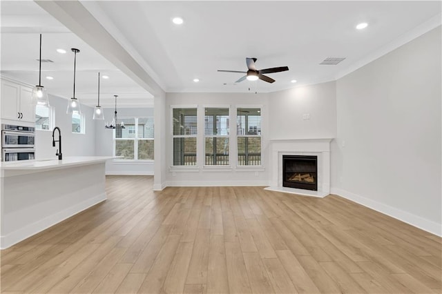 unfurnished living room with ornamental molding, sink, ceiling fan with notable chandelier, and light hardwood / wood-style flooring