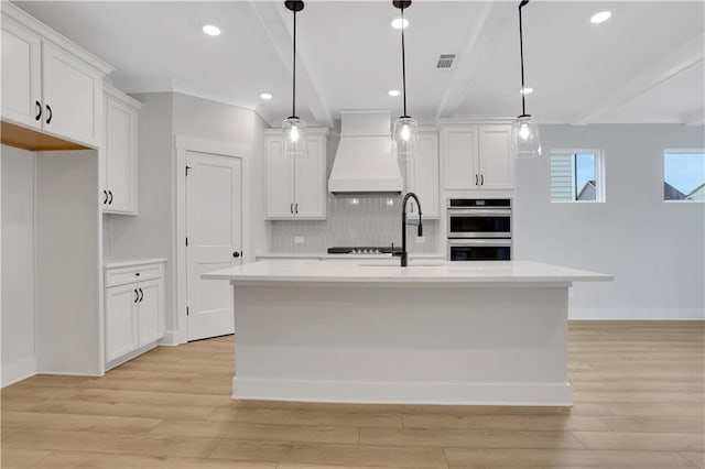 kitchen featuring white cabinetry, custom range hood, and a center island with sink