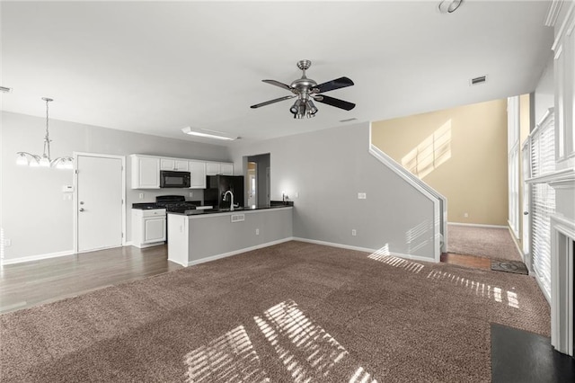 unfurnished living room featuring dark colored carpet, visible vents, baseboards, and ceiling fan with notable chandelier