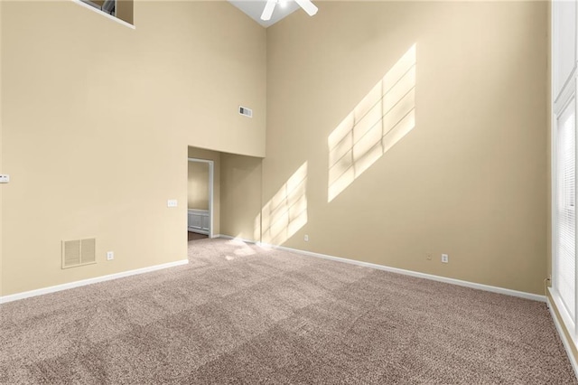 carpeted spare room with visible vents, baseboards, and a towering ceiling