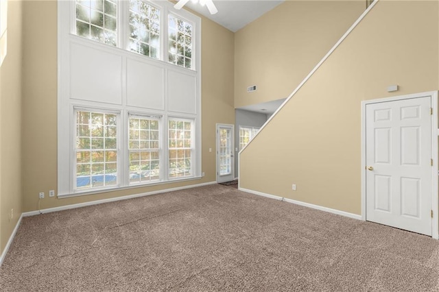 unfurnished living room featuring visible vents, a ceiling fan, carpet, baseboards, and a towering ceiling