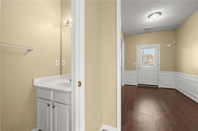 bathroom featuring visible vents, a wainscoted wall, vanity, wood finished floors, and a textured ceiling