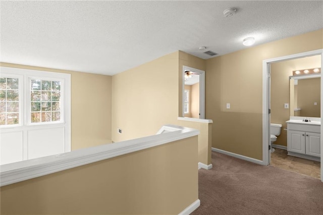 corridor featuring visible vents, an upstairs landing, a textured ceiling, carpet, and baseboards