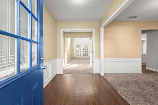 foyer entrance with a textured ceiling, dark wood-style floors, visible vents, wainscoting, and a decorative wall