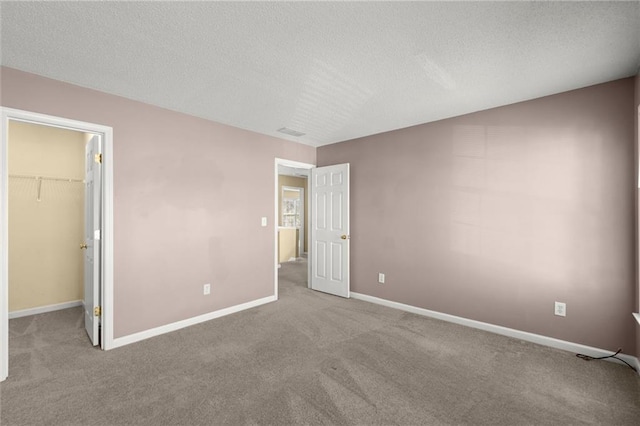 unfurnished bedroom featuring visible vents, a walk in closet, baseboards, carpet flooring, and a textured ceiling